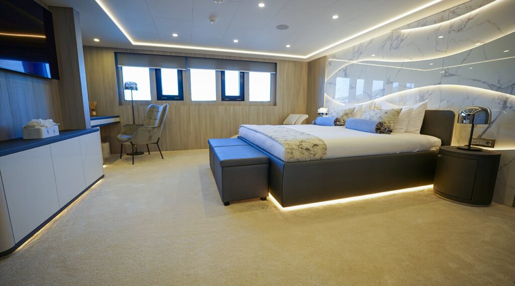 large bed in a yacht cabin with windows, work desk, wide screen tv